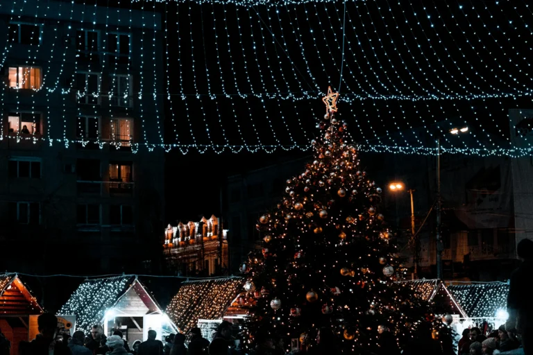 Lit Christmas tree and festive string lights at a night market with wooden stalls